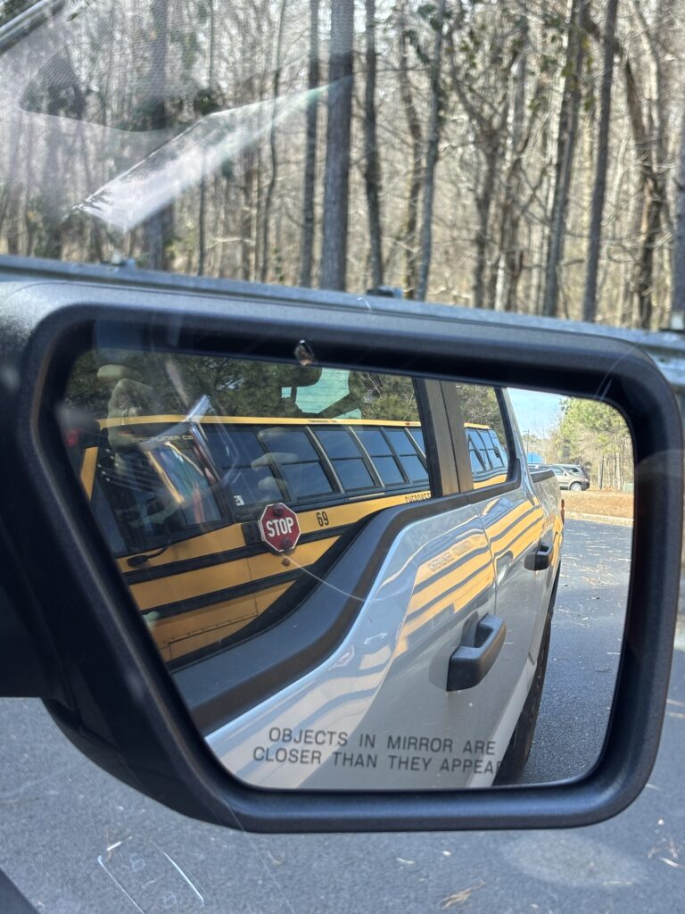 A driver's side mirror with the reflection of a bus